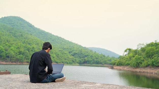 Młody mężczyzna pracujący na laptopie i siedzący na łonie natury Koncepcja Workation and Digital Nomad