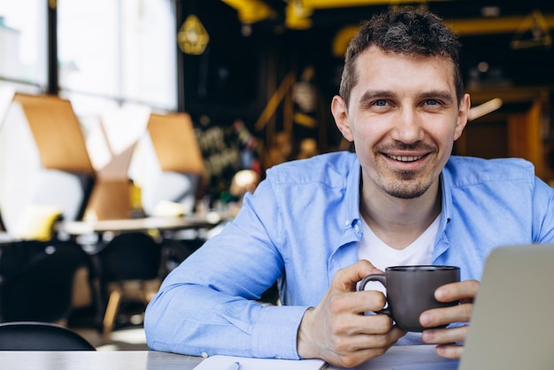 Młody mężczyzna pracujący na laptopie w kawiarni