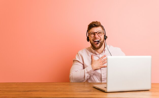 Młody Mężczyzna Pracujący W Call Center śmieje Się Głośno, Trzymając Rękę Na Piersi.