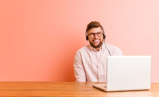 Młody Mężczyzna Pracujący W Call Center śmieje Się I Zamyka Oczy, Czuje Się Zrelaksowany I Szczęśliwy.