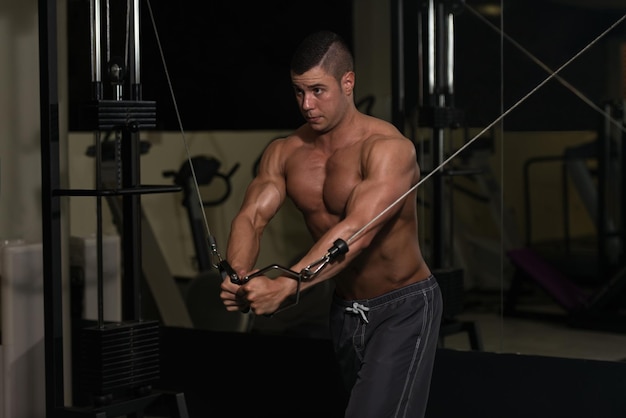 Młody mężczyzna pracuje nad klatką piersiową ze skrzyżowaniem kabli w nowoczesnej siłowni
