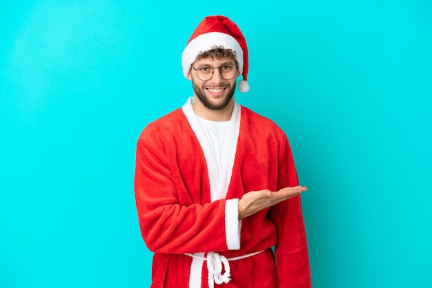 Młody mężczyzna przebrany za Świętego Mikołaja na niebieskim tle przedstawiający pomysł, patrząc w kierunku uśmiechu