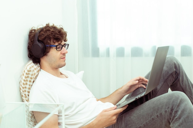 Młody mężczyzna rasy kaukaskiej pracuje z domu na laptopie i łączy się online z biurem w pomieszczeniu, aby uzyskać zdalne miejsce pracy w Internecie Młody dorosły mężczyzna jest niezależny, pracuje inteligentnie na notebooku, siedząc na łóżku, sypialnia