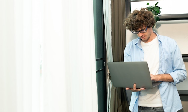 Młody mężczyzna rasy kaukaskiej pracuje z domu na laptopie i łączy się online z biurem w pomieszczeniu w celu zdalnego dostępu do Internetu Młody dorosły mężczyzna jest niezależny, pracuje mądrze na notebooku, siedzi w pokoju roboczym