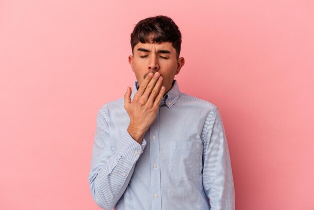 Młody mężczyzna rasy mieszanej odizolowany na różowym tle ziewający pokazujący zmęczony gest zakrywający usta dłonią