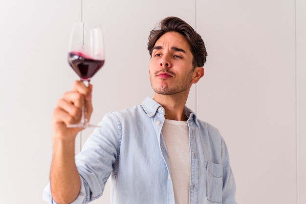 Młody mężczyzna rasy mieszanej pijący wino w kuchni