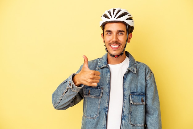 Młody Mężczyzna Rasy Mieszanej W Kasku Rowerowym Na żółtym Tle Uśmiechający Się I Podnoszący Kciuk W Górę