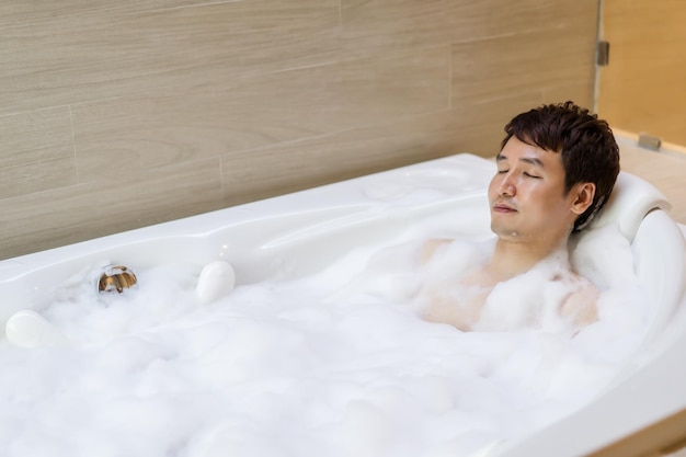 Młody mężczyzna relaksuje się w wannie z zamkniętymi oczami w łazience