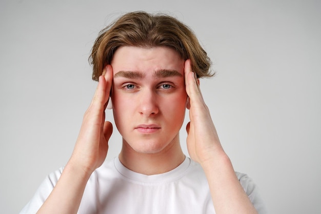 Młody mężczyzna ściska głowę, najwyraźniej z powodu dyskomfortu lub stresu, na neutralnym tle