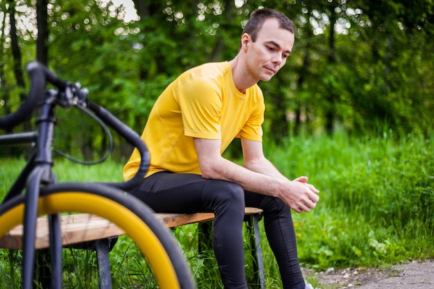 Młody mężczyzna siedzący na ławce w publicznym parku komunikuje się przez telefon komórkowy