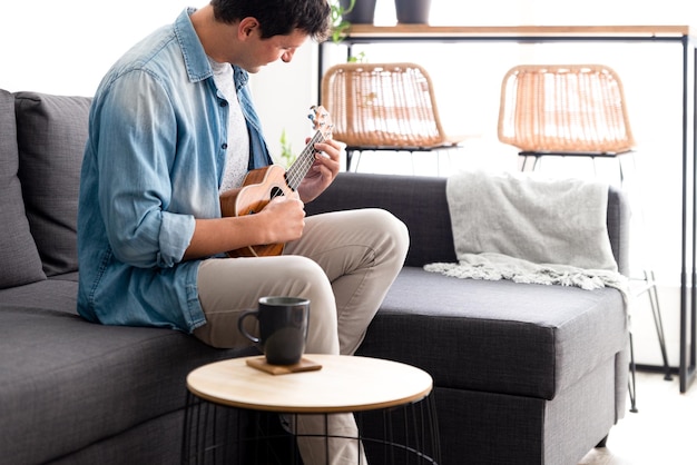 Młody mężczyzna siedzi na kanapie grając na ukulele