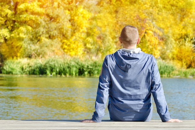 Młody mężczyzna siedzi na pomoście Jesienny słoneczny widok z tyłu