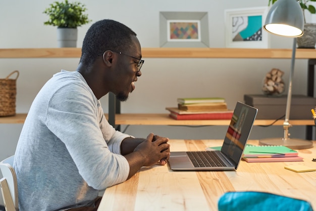 Młody mężczyzna siedzi przy stole i rozmawia online ze swoim przyjacielem na laptopie