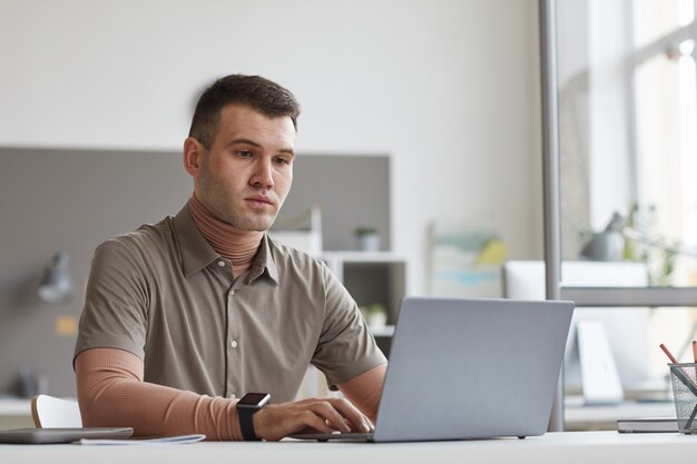 Młody mężczyzna siedzi w swoim miejscu pracy i wpisując na laptopie on pracuje online w biurze