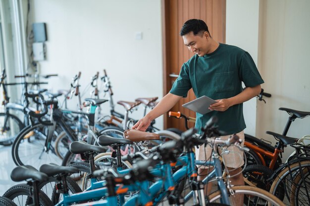 Młody mężczyzna sprawdza siodełko nowego roweru, korzystając z tabletu w sklepie rowerowym