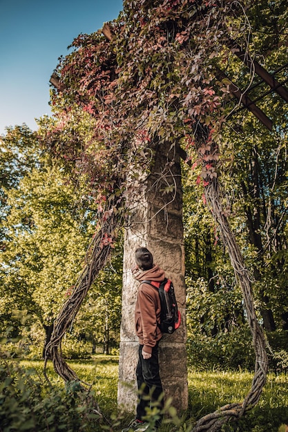 Zdjęcie młody mężczyzna stoi w pobliżu starej kolumny pokrytej drzewami