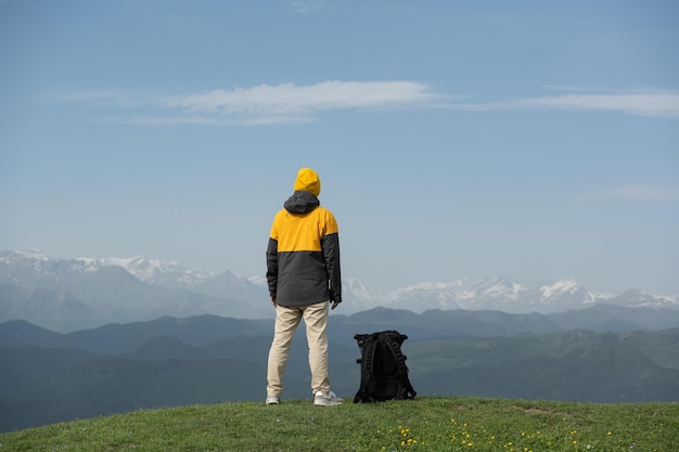 Młody mężczyzna stojący na szczycie góry, podziwiając malowniczy widok na ośnieżone szczyty pasma górskiego