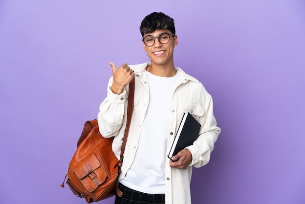 Młody mężczyzna student na pojedyncze fioletowe tło, wskazując na bok, aby przedstawić produkt