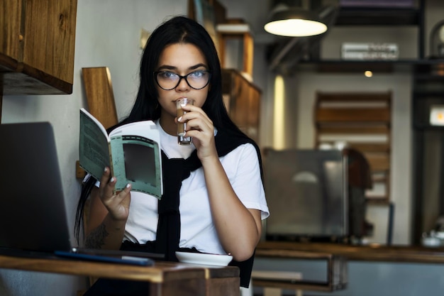 Zdjęcie młody mężczyzna studiujący na swoim laptopie, czytający książkę i pijący kawę, bloger, student projektowania, spóźniony