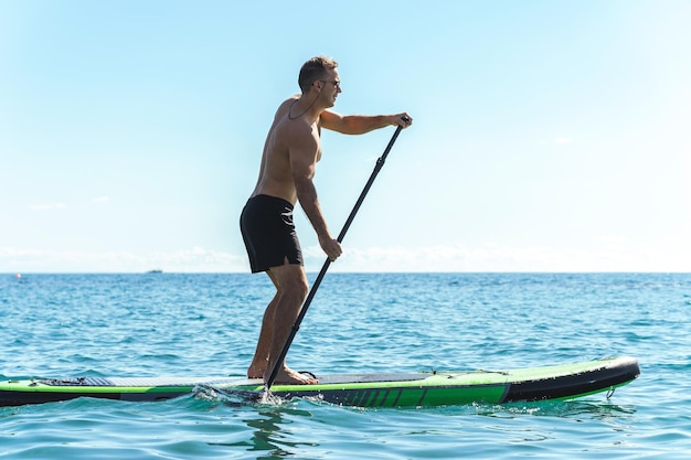 Młody mężczyzna surfer jeżdżący na desce wiosłowej w oceanie