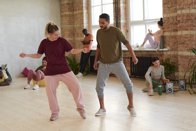 Młody mężczyzna tańczy razem z kobietą w studio tańca z innymi ludźmi relaks