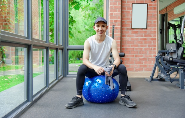 Młody mężczyzna trenuje równowagę z piłką do jogi w sportowej siłowni rehabilitacyjnej