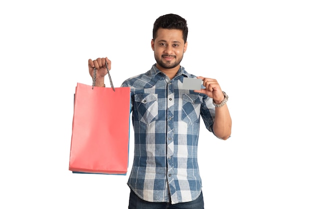 Młody mężczyzna trzyma i pozuje z torbami na zakupy z kartą kredytową lub debetową na białym tle