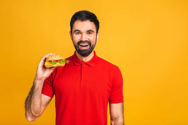 Młody mężczyzna trzyma kawałek kanapki. Student je fast food. Burger nie jest pomocnym jedzeniem.