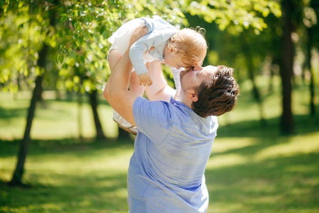 Młody mężczyzna trzyma małą córeczkę w ramionach w parku