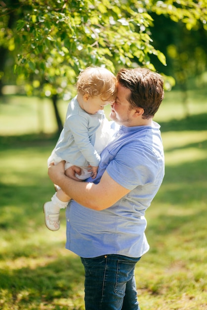 Młody mężczyzna trzyma małą córeczkę w ramionach w parku
