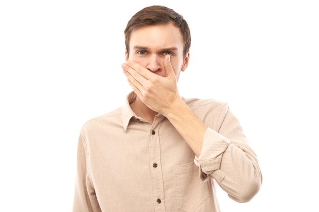 Młody mężczyzna trzyma nos, aby uniknąć zdegustowanego zapachu, szczypie nos i usta palcami i wstrzymuje oddech na białym tle