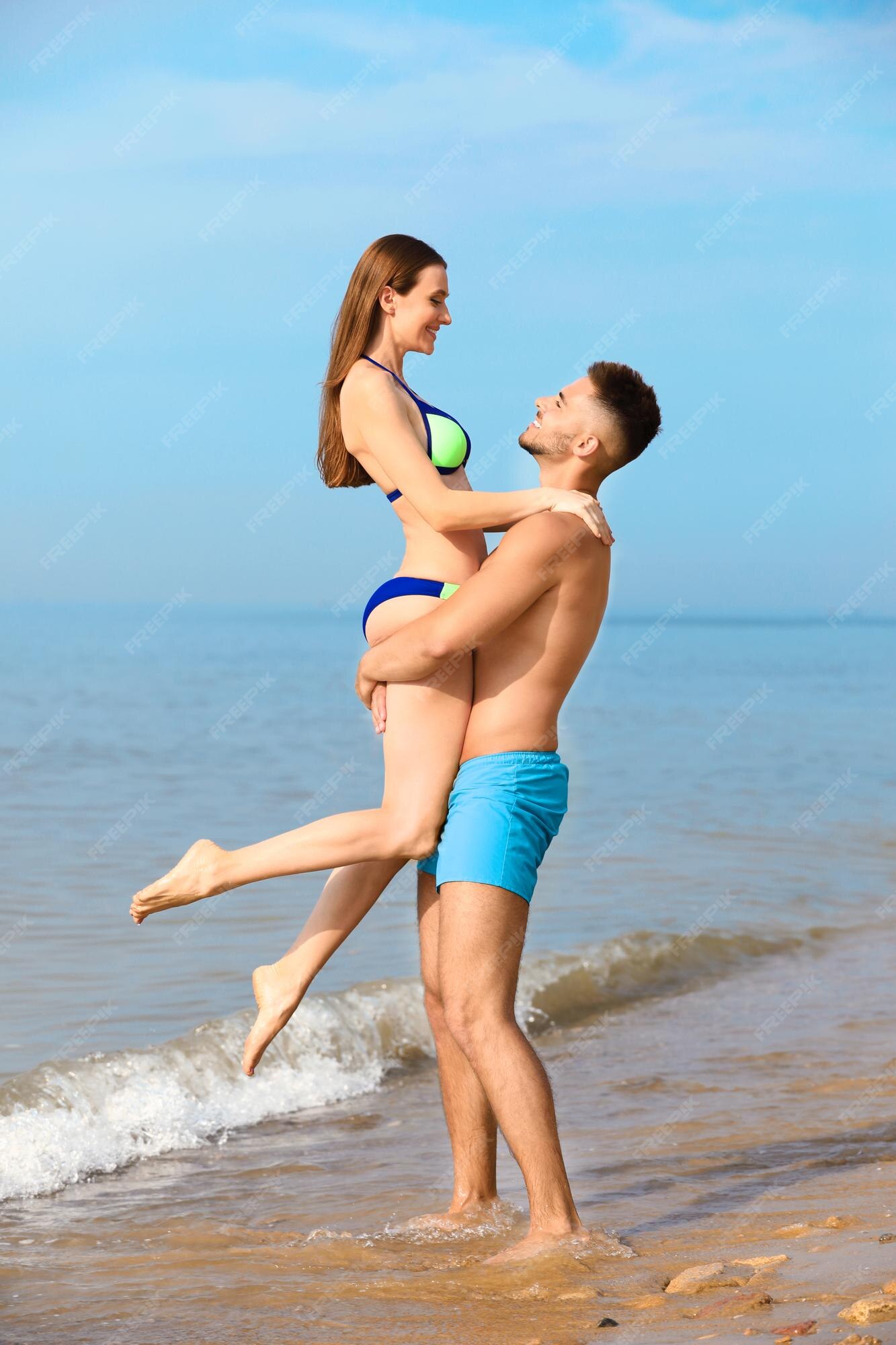 Młody Mężczyzna Trzyma Swoją Dziewczynę W Bikini Na Plaży Urocza Para |  Zdjęcie Premium