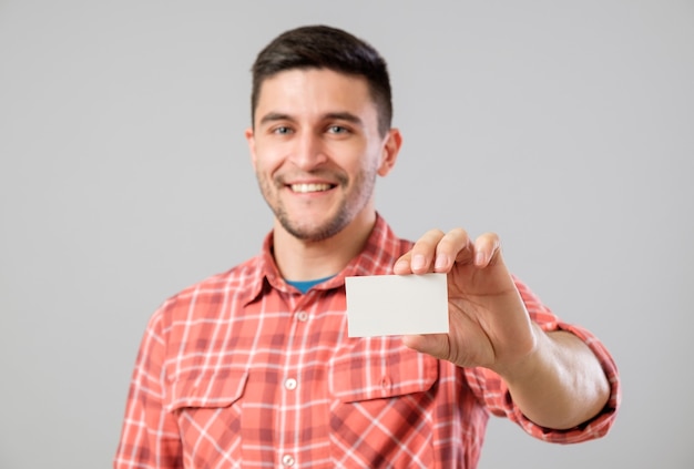 Młody mężczyzna trzymający i pokazujący pustą wizytówkę odizolowaną na szarym tle