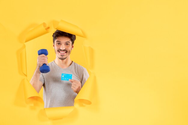 młody mężczyzna trzymający kartę kredytową i hantle na żółtym tle pieniądze pasują do sportowca