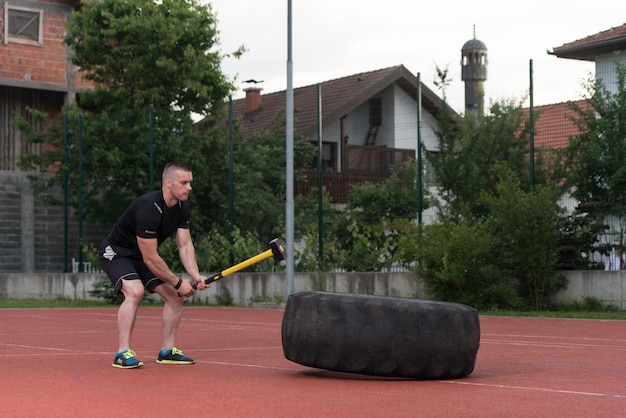 Młody mężczyzna uderza w oponę - trening na świeżym powietrzu z młotkiem i oponą ciągnika