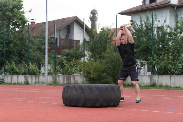 Młody mężczyzna uderza w oponę - trening na świeżym powietrzu z młotkiem i oponą ciągnika