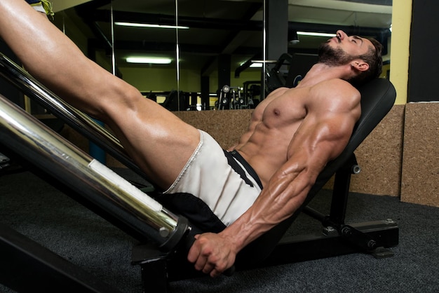 Młody mężczyzna używający maszyny do wyciskania nóg w klubie fitness na siłowni