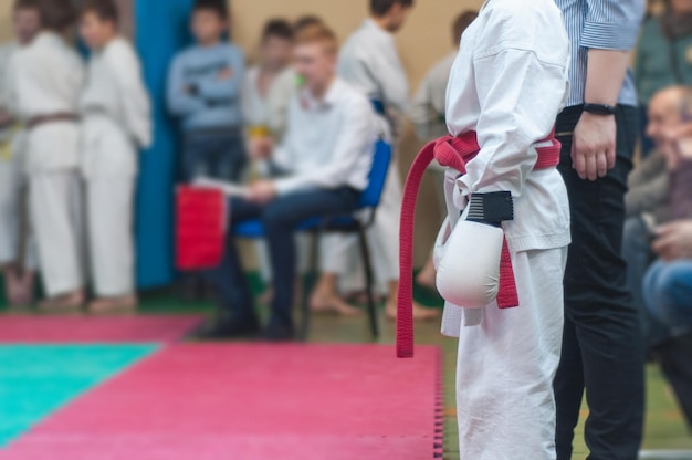 Młody Mężczyzna W Białym Mundurze Z Czerwonym Pasem I Rękawiczkami Przygotowuje Się Do Treningu Karatedo Bojowego I Zdrowego Stylu życia