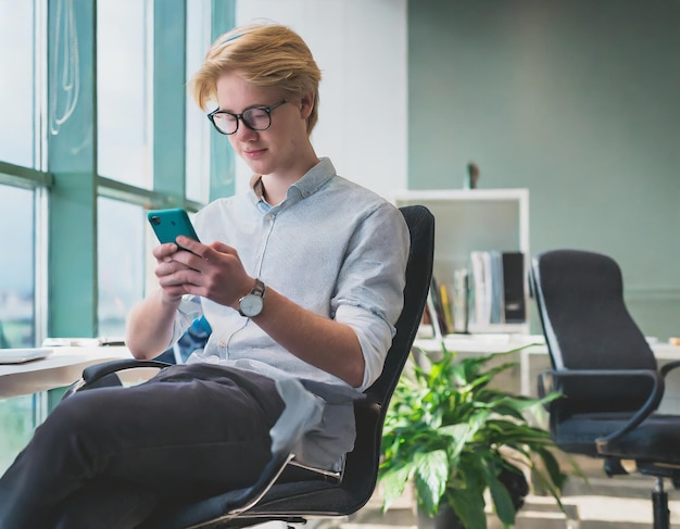 Zdjęcie młody mężczyzna w biurze siedzący na krześle używający smartfona