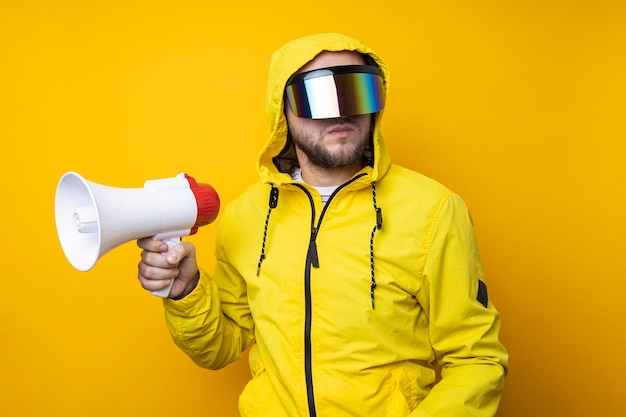 Młody mężczyzna w cyberpunkowych okularach trzymający megafon na żółtym tle