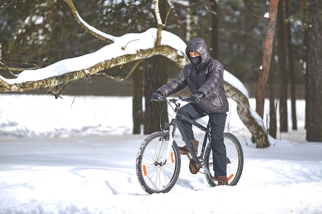 Młody mężczyzna w czarnym ubraniu jeździ na rowerze po śniegu