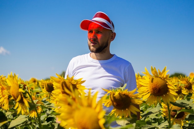Młody mężczyzna w czerwonej osłonie przeciwsłonecznej na głowie na polu słoneczników w pogodny dzień