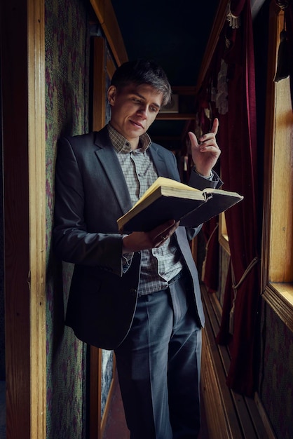 Młody mężczyzna w garniturze stoi w korytarzu starego rzadkiego wagonu i czyta książkę