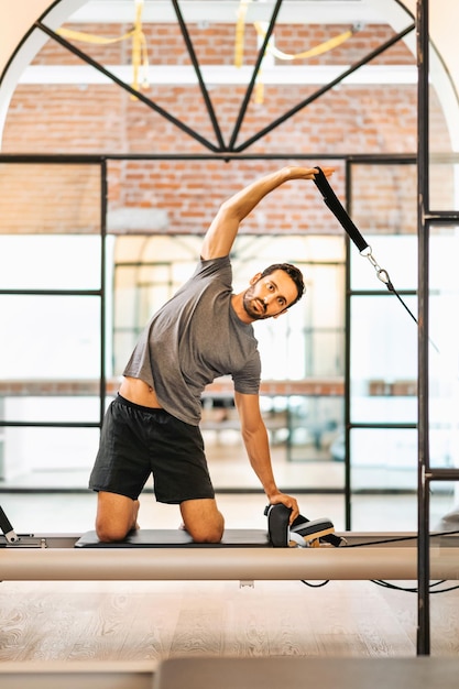 Młody mężczyzna w odzieży sportowej ćwiczy pilates i rozciąga się na łóżku reformatora