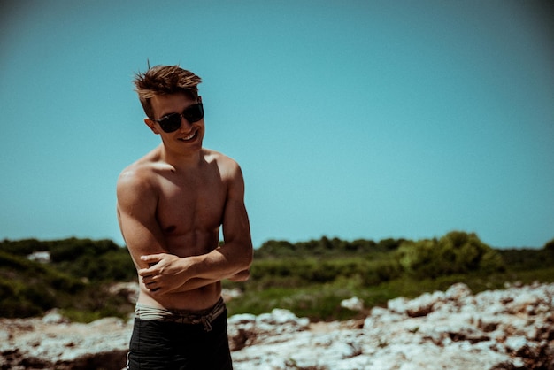 Młody mężczyzna w okularach przeciwsłonecznych stoi na plaży przed czystym niebem