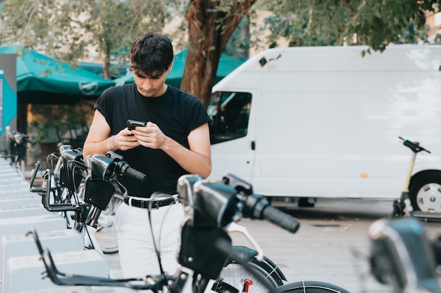 Młody mężczyzna w wypożyczalni rowerów sprawdza instrukcje na telefonie, aby wypożyczyć rower podczas wycieczki po mieście. Kopiuj obraz miejsca. Koncepcja stylu życia miasta, 0 emisji zielony transport bez paliwa.