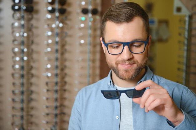 Młody mężczyzna wybiera okulary w sklepie optycznym