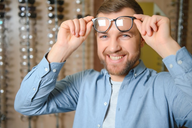 Młody mężczyzna wybiera okulary w sklepie optycznym