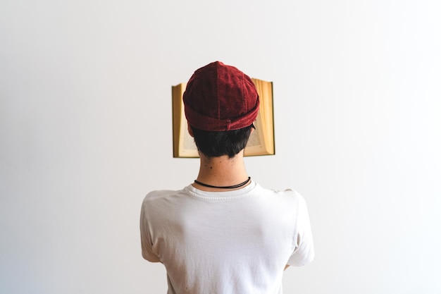 Młody mężczyzna z Ameryki Łacińskiej leży na plecach w czapce i czyta książkę na białym tle Artystyczne zdjęcie