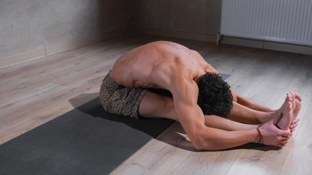 Zdjęcie młody mężczyzna z gołym tułowiem praktykujący jogę wykonujący ćwiczenia na matce jogi